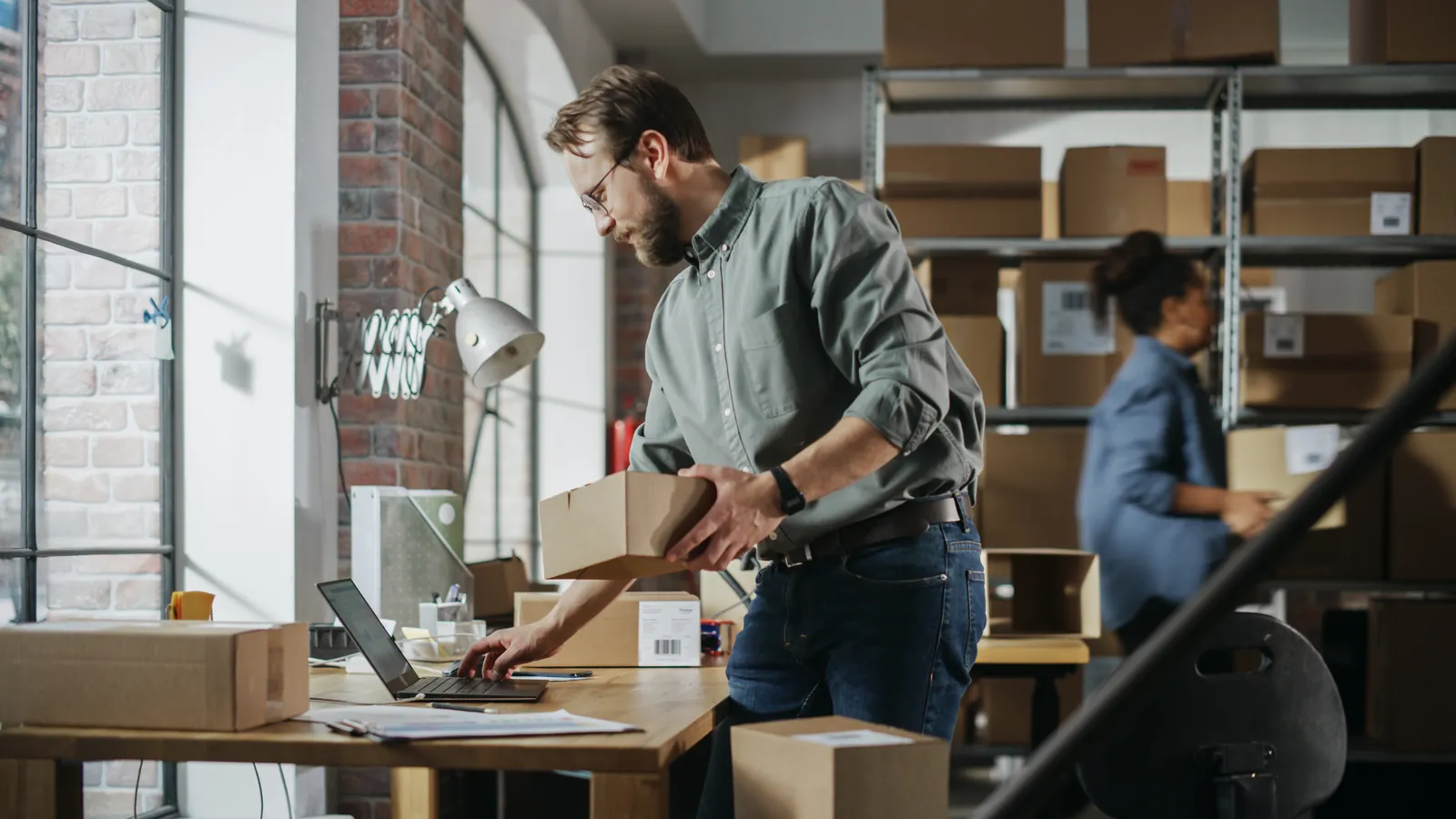 Staff prepare parcels in a storeroom with cardboard boxes and a laptop.